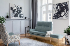 Stylish scandinavian home interior of living room with design gray sofa, armchair, marble stool, black coffee table, modern paintings, decoration, plant and elegant personal accessories in home decor.